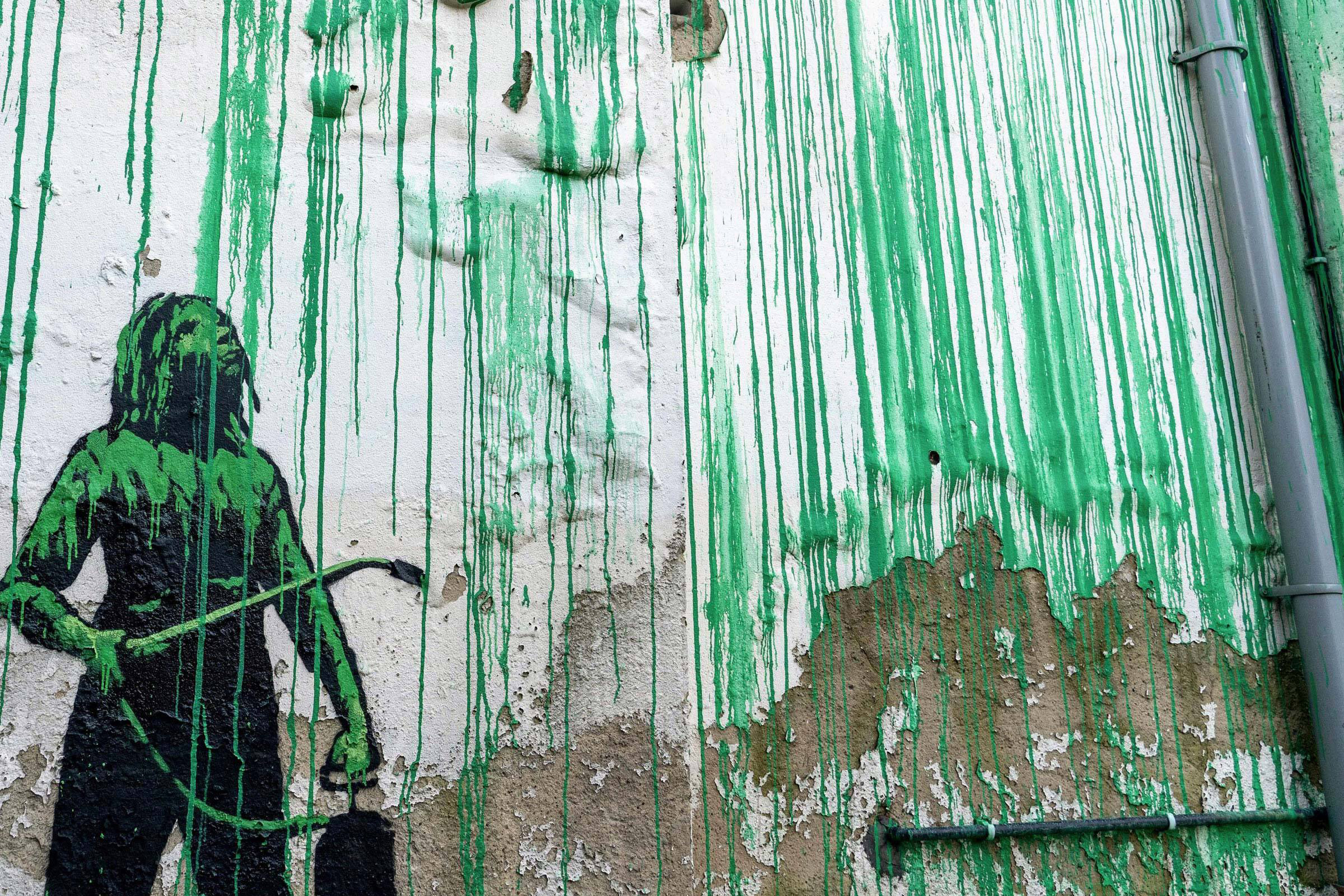 Close-up of Banksy's mural, detailing dripping bright green paint.