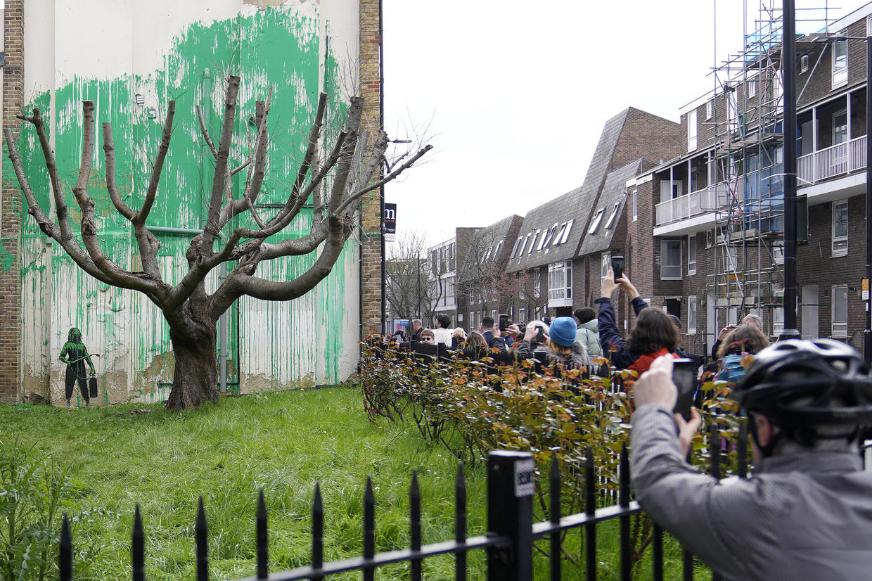 A crowd of people are standing and taking photos of Banksy's mural on the wall of a housing complex.