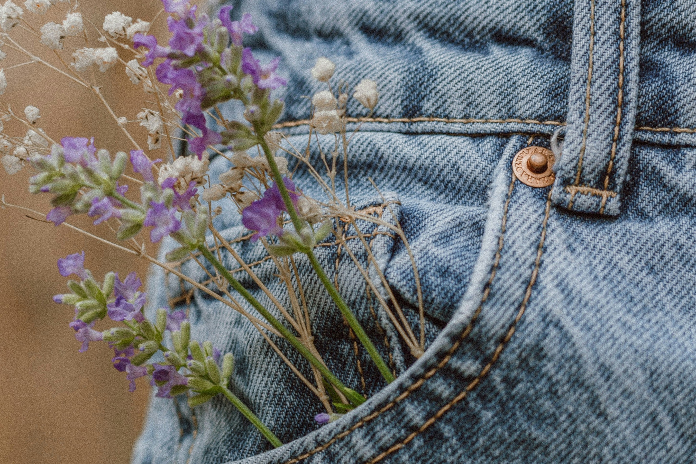 Close-up of a pair of light-wash denim jeans with flowers in the pocket.